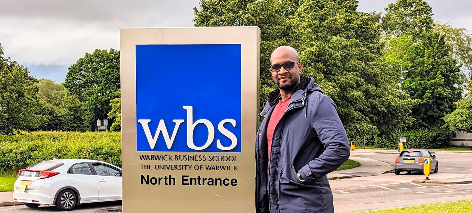 Robert Ndebele stands next to the Warwick Business School logo outside the School
