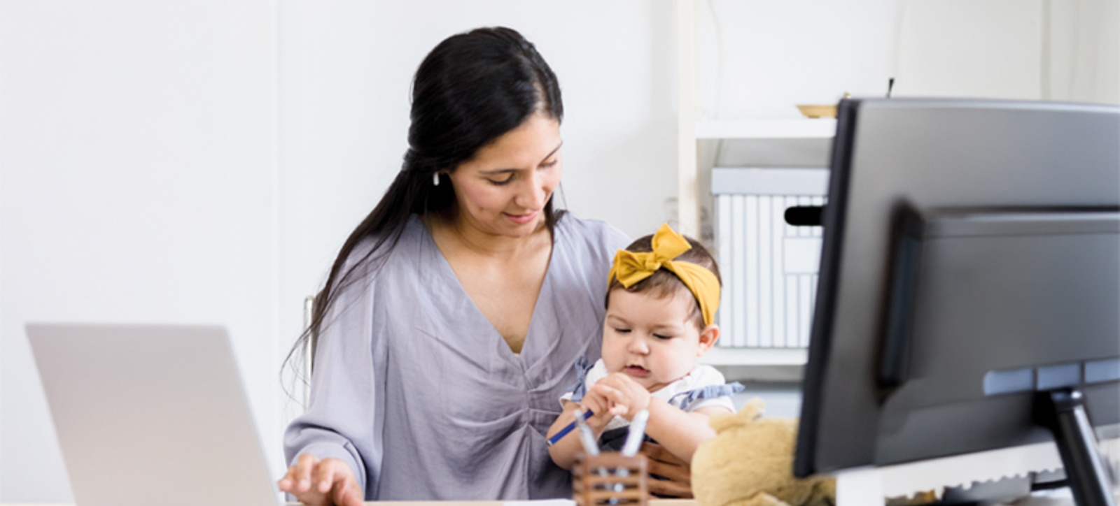 A hybrid worker sits at her computer at home with her baby on her lap while she works.