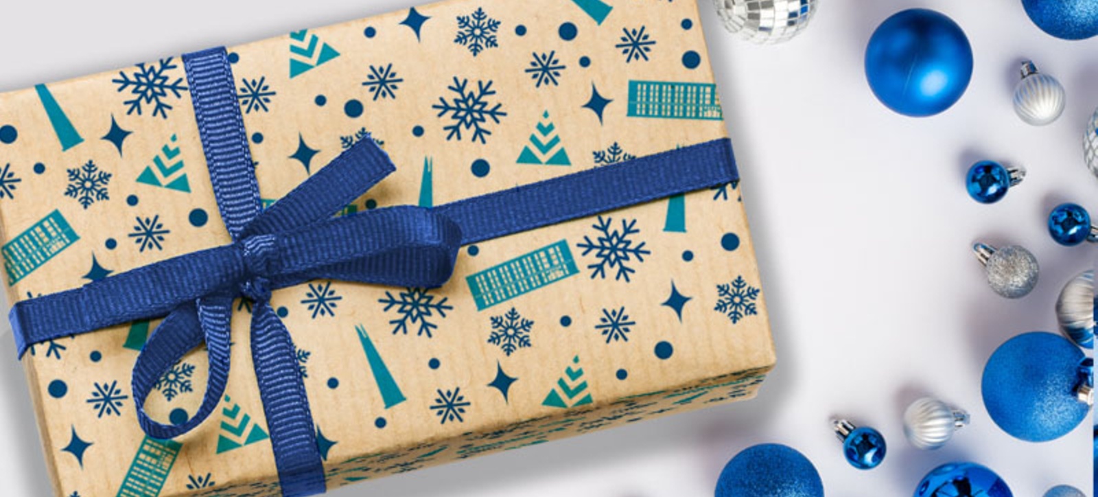 A Christmas present wrapped in Warwick Business School themed paper and a blue bow, surrounded by blue and silver baubles.