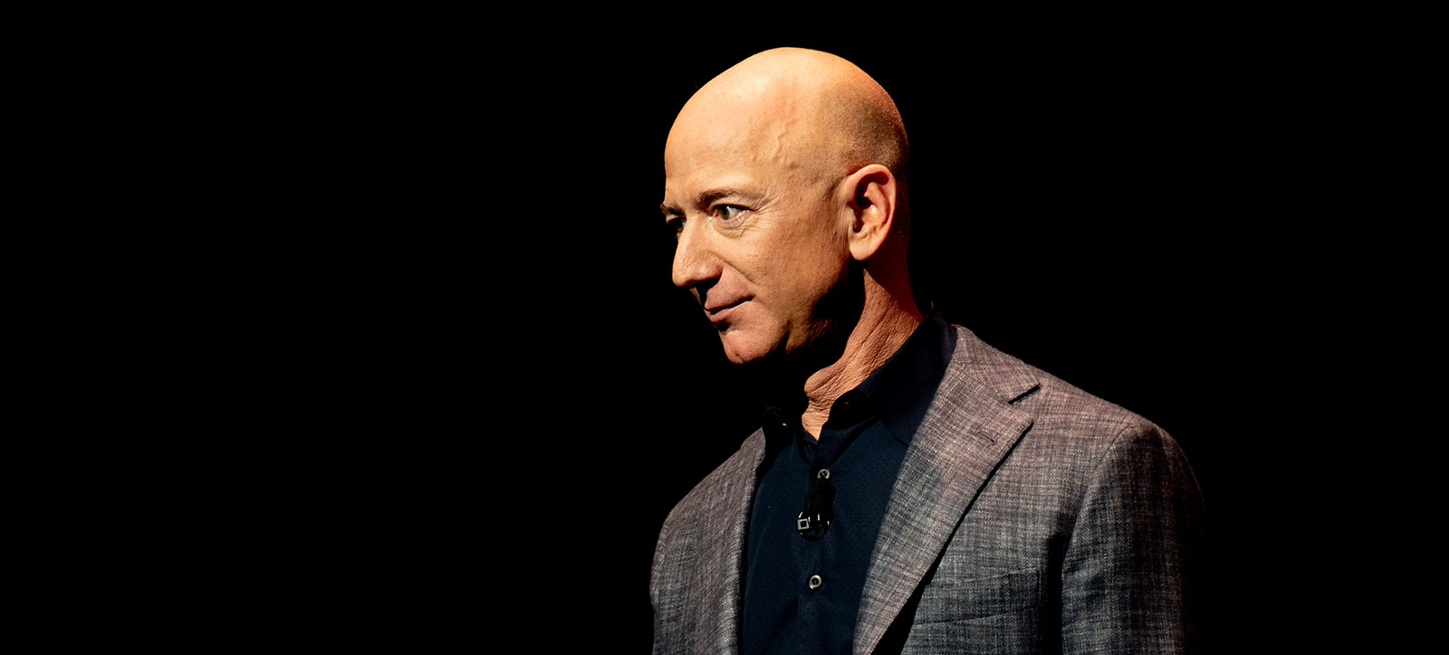 A photograph of Amazon founder Jeff Bezos on stage against a dark backdrop. Photograph credited to Daniel Oberhaus, 2019