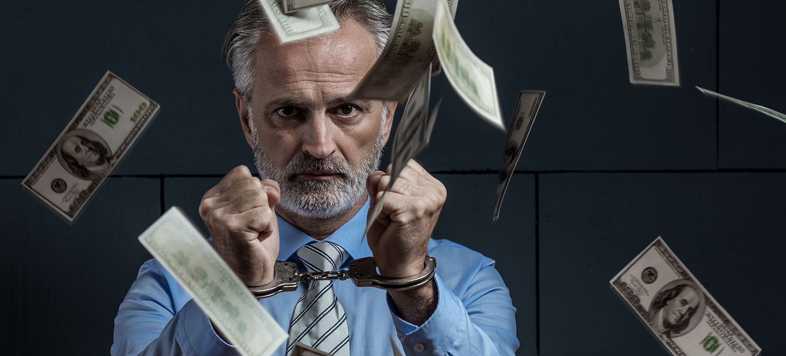 A businessman in a shirt and tie wearing handcuffs in a prison cell as dollar bills fall around him