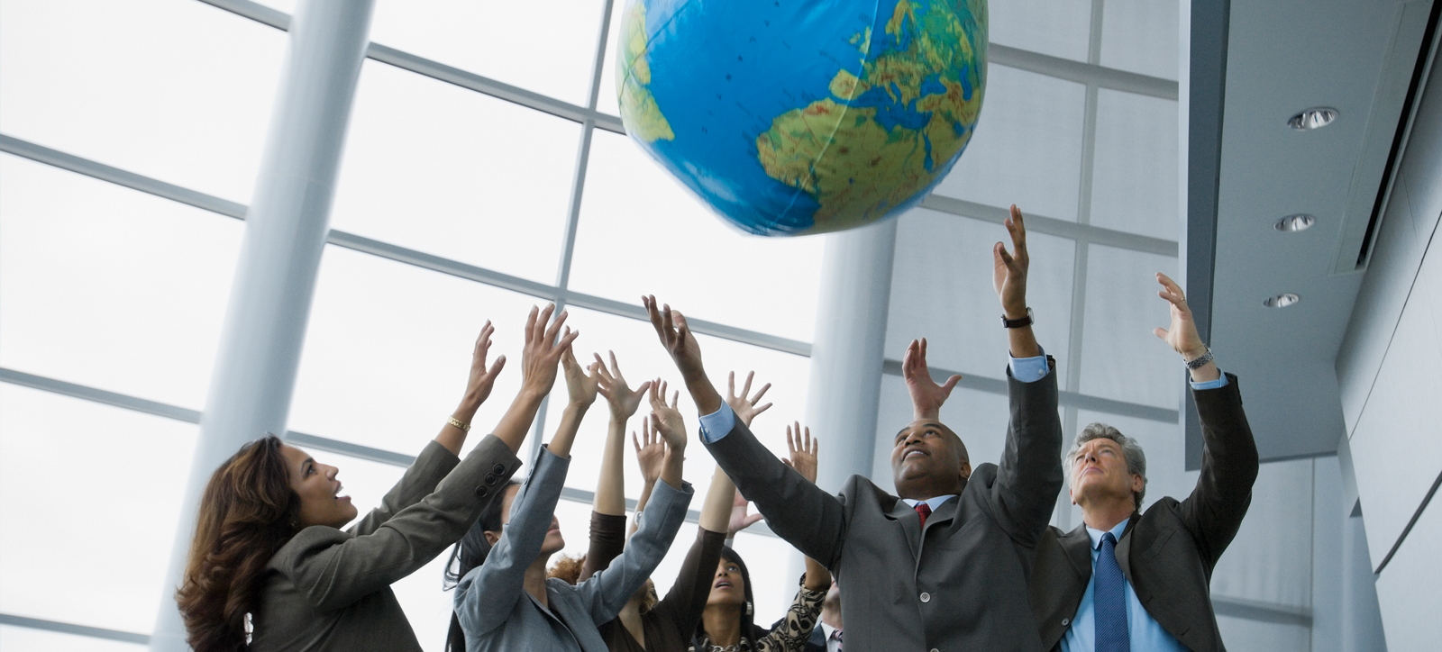 A diverse group of business men and women with their arms in their air to catch and inflatable global representing environmental and social issues