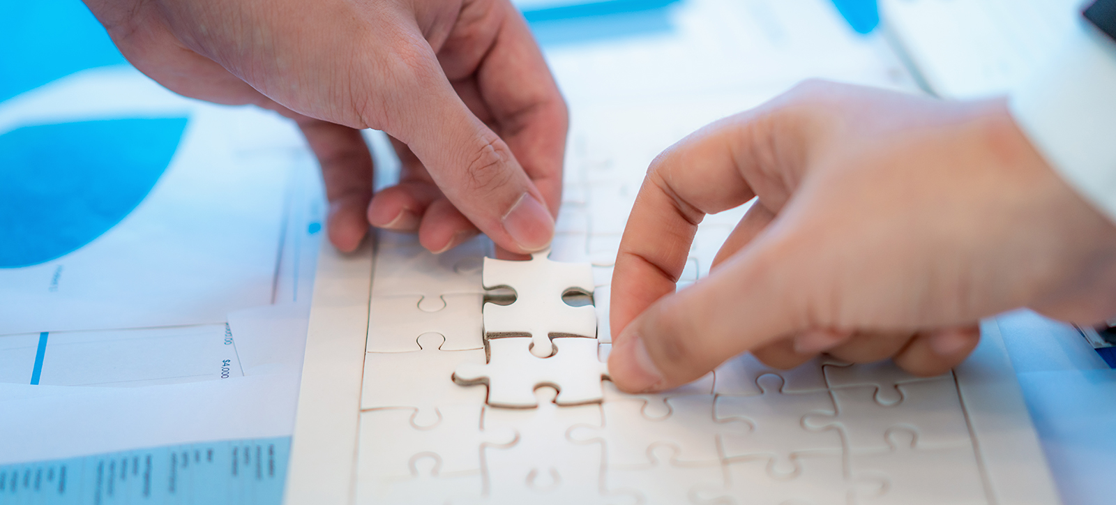 A close up of two hands building a jigsaw on top of pages of printed data laid out on a desk