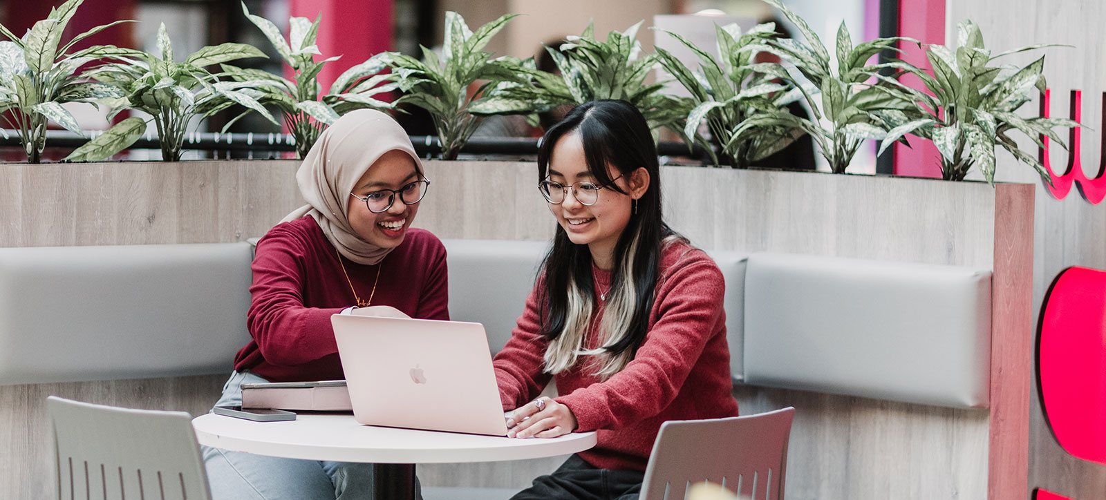 Two Warwick Business School students sat at a laptop discussing the article they are working on.